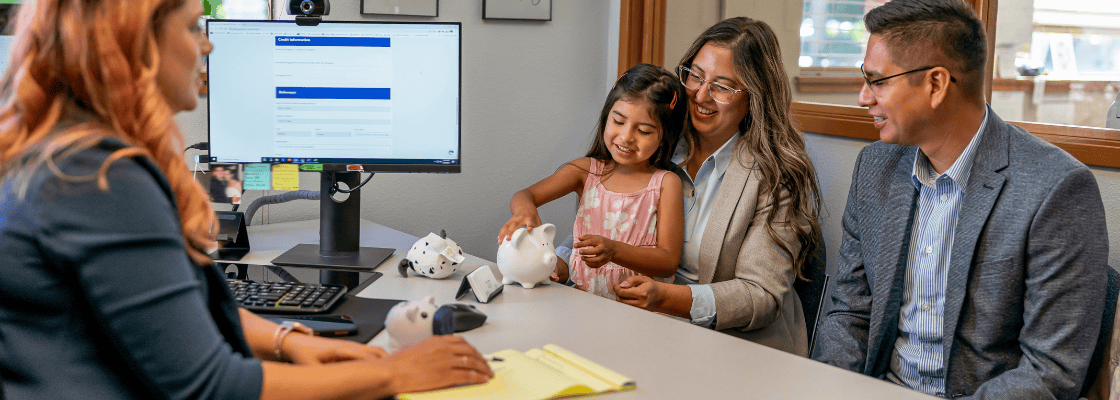 a woman and a girl sitting at a desk with a piggy bank