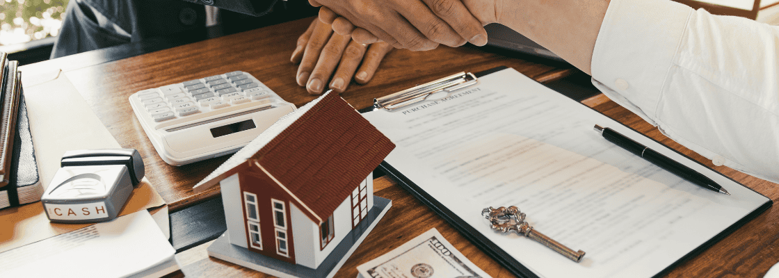 a couple hands shaking hands next to a house model